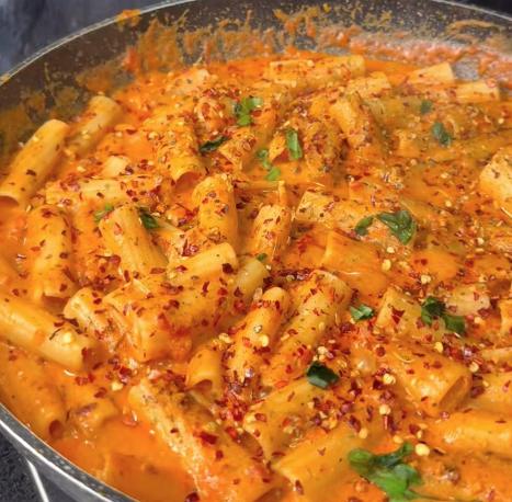 Bord met pasta in romige tomatenroomsaus, gegarneerd met verse basilicum en kaas