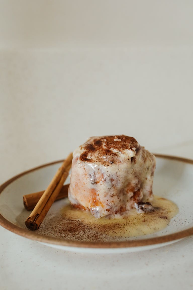 Close-up of a frosted cinnamon roll with cinnamon sticks on a plate. Perfect for dessert and food styling.